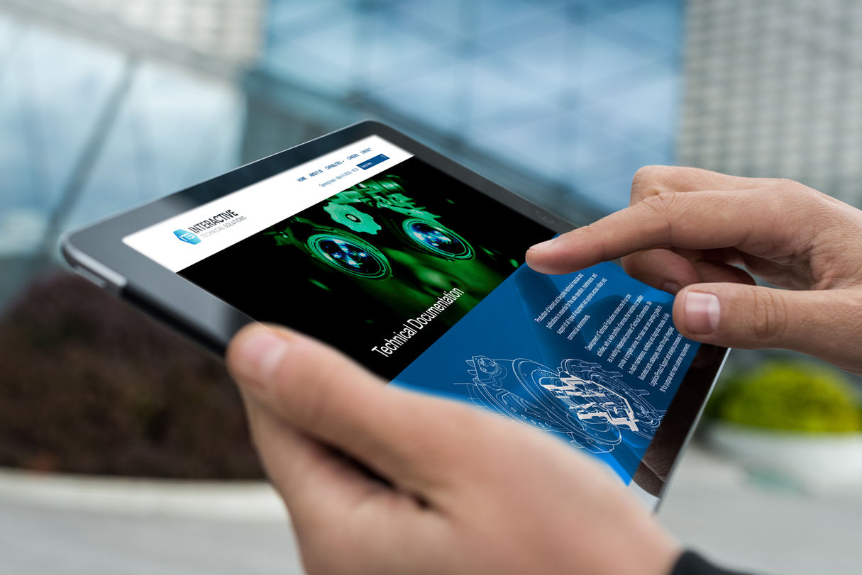 Hands holding a tablet displaying the Interactive Technical Solutions website, featuring technical documentation imagery, blue corporate design elements and clean professional layout.