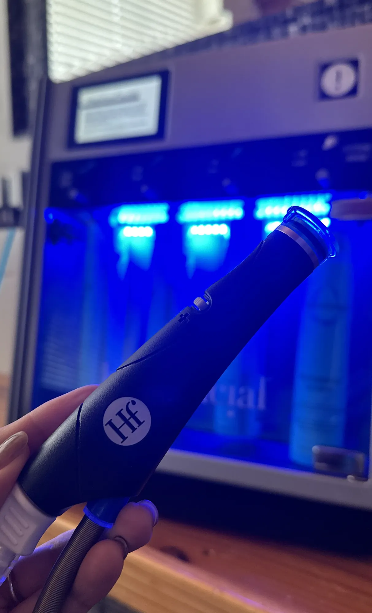 Close-up of a hand holding the HydraFacial treatment wand in front of the machine’s blue LED lights.