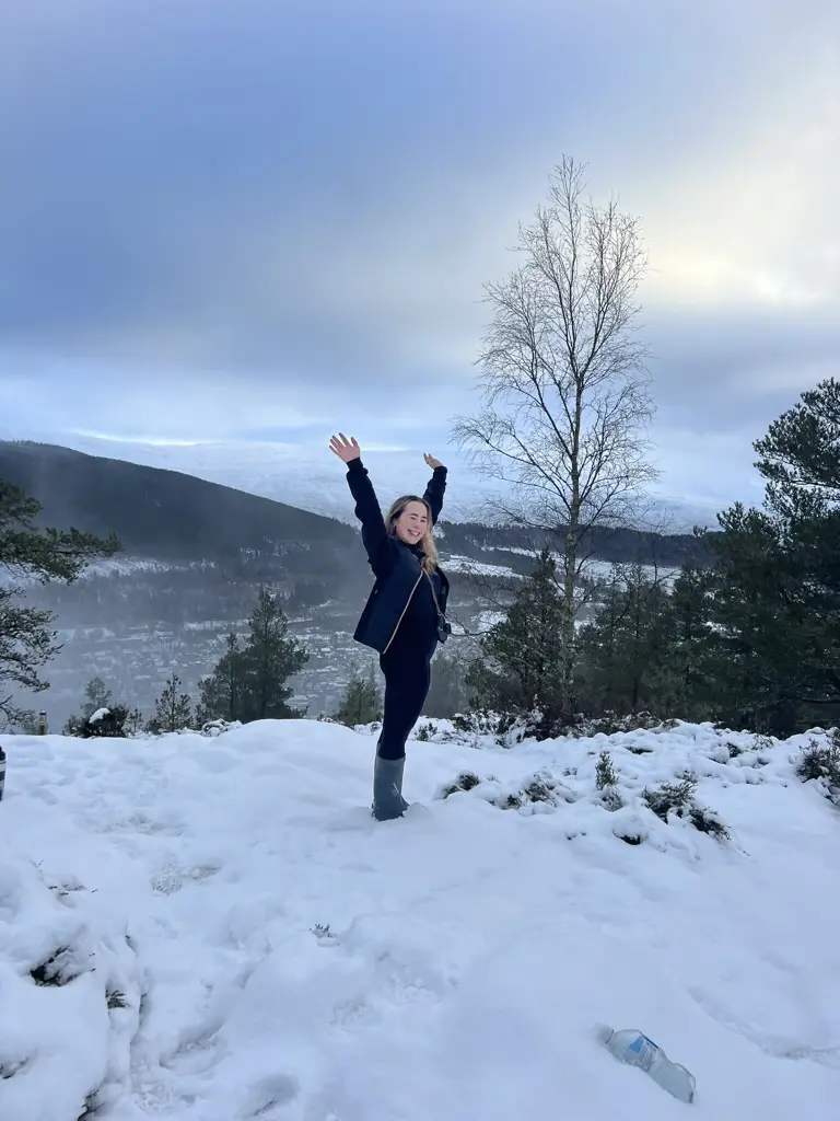 girl with arms in air smiling at top of mountain in snow in ballater scotland