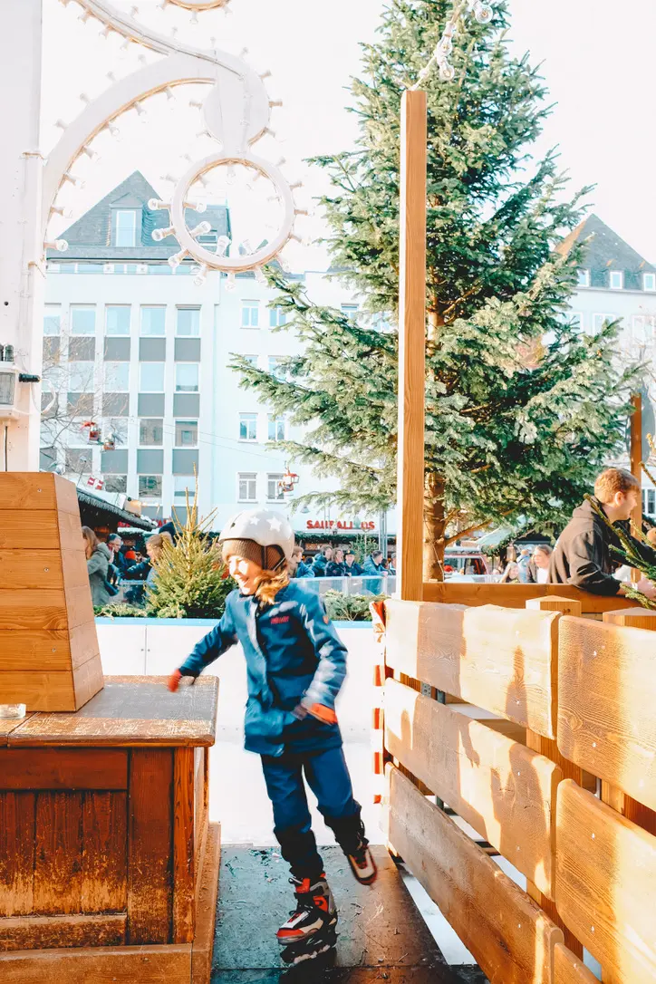 kid ice skating with christmas tree in background