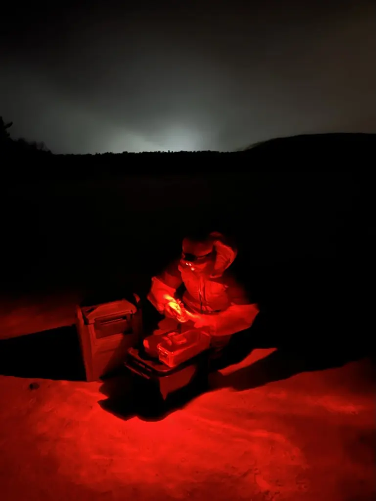 man wearing head torch making hot chocolate in snow