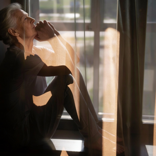 Older woman sitting by a window, reflecting about traveling alone after 60