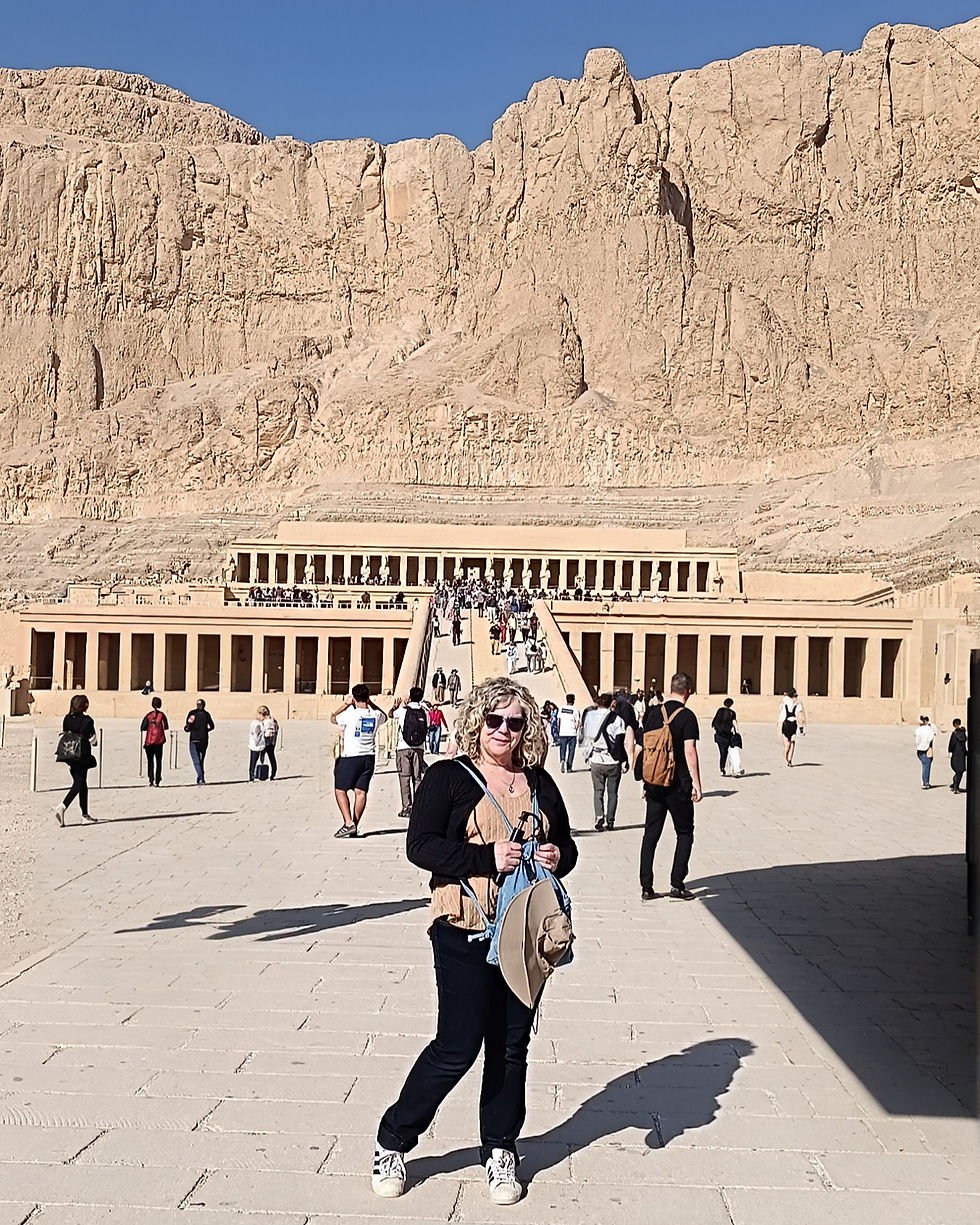 Woman standing in front of an ancient Egyptian temple carved into sandstone, warm sunset light.