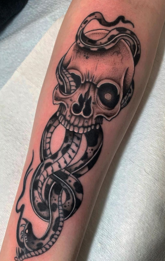 Skull entwined with a coiling serpent, tattooed on a forearm