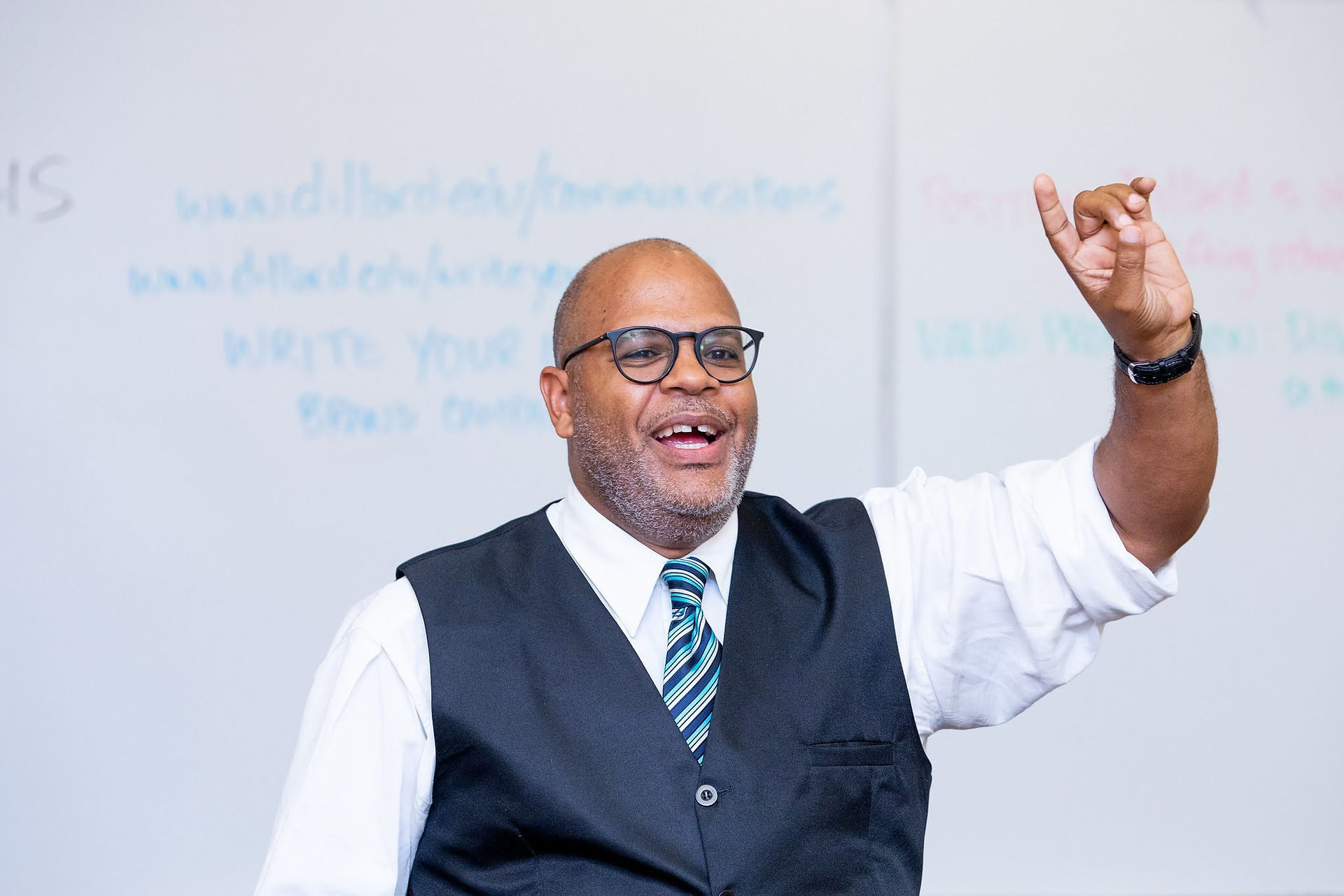 A smiling man speaking with his arm held up as if he is making a point