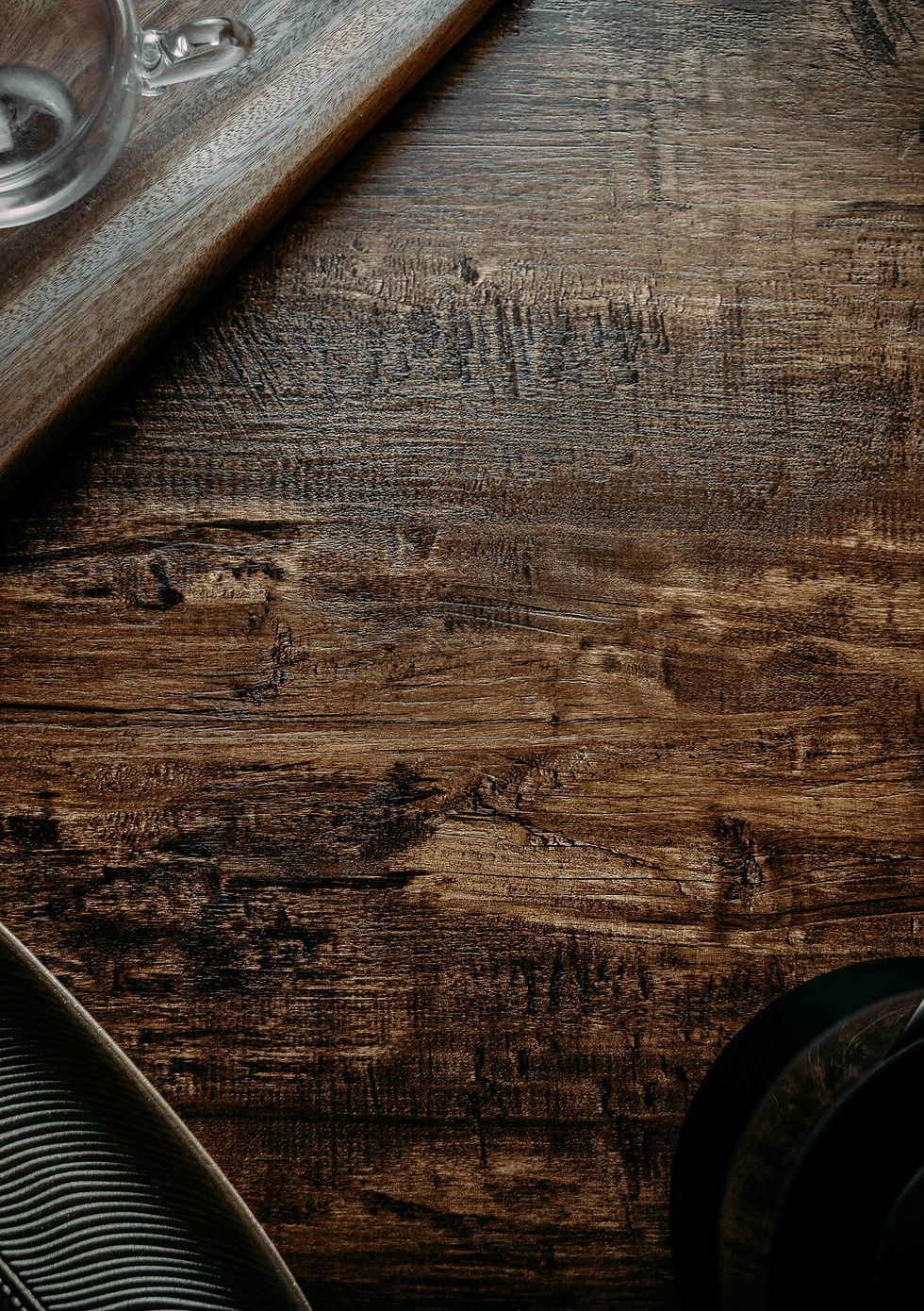 Wooden tabletop with a teacup and wooden tray in the corner. Dark, rich grain texture dominates, creating a warm and rustic feel.