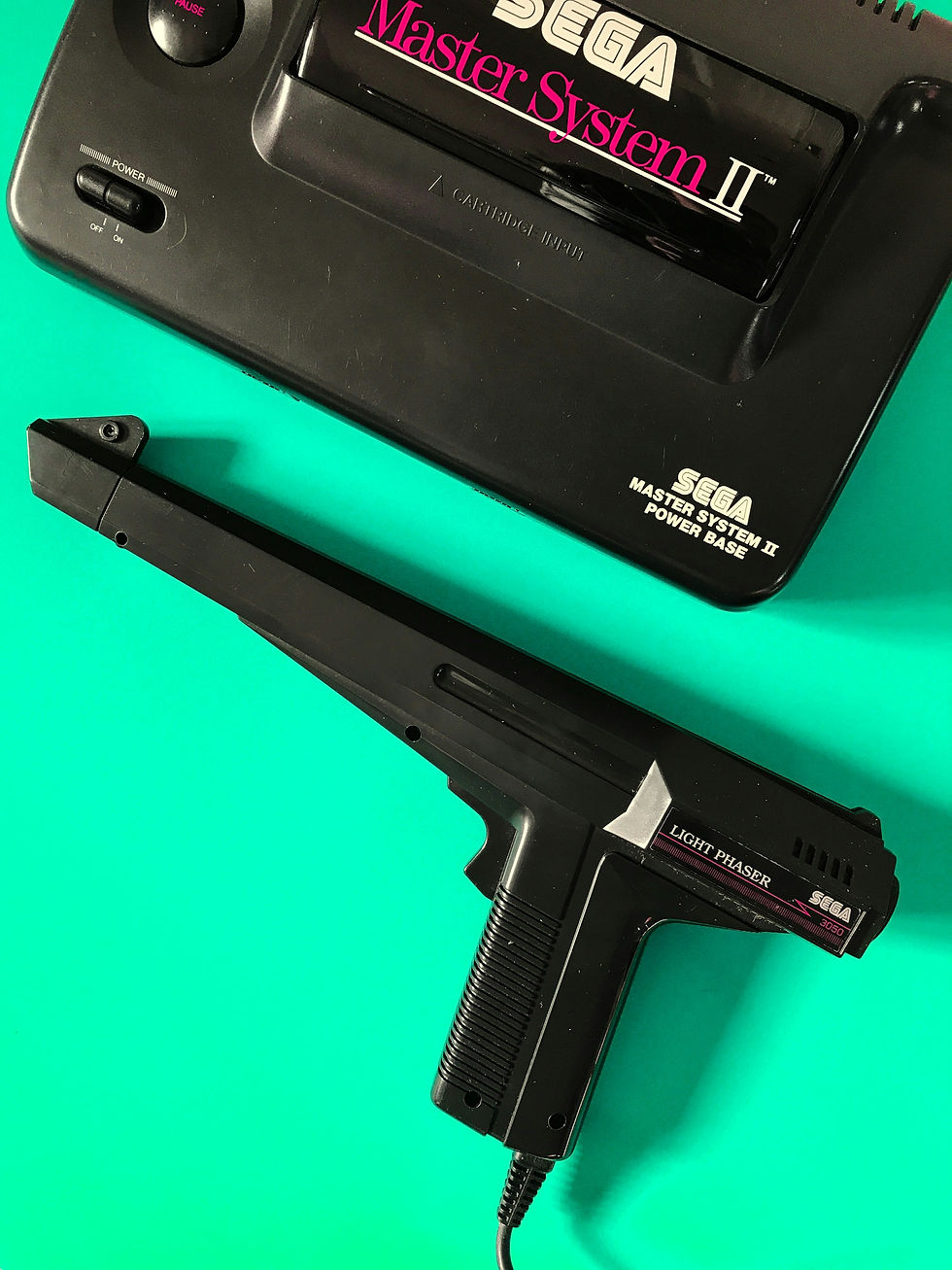 Black Sega Master System II with a light gun on a bright teal background. Visible text: "SEGA Master System II Power Base," "Light Phaser."