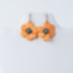 Orange flower earrings with turquoise centers displayed on a white mannequin.