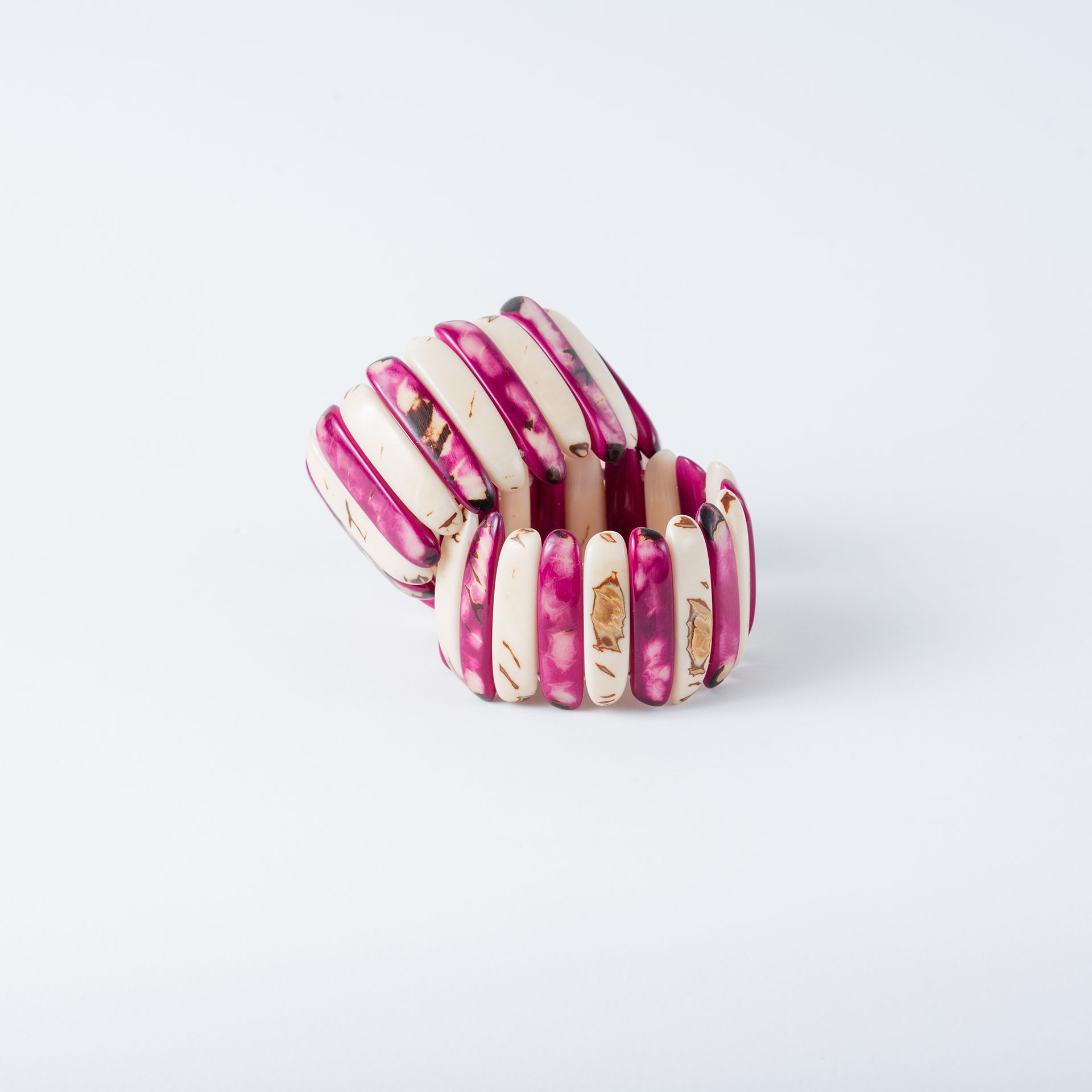 Two magenta and white elastic threaded tagua bracelets on a white background. lightweight, handcrafted, fashion ecofriendly jewelry made from natural and organic tagua nut.