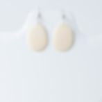 Pair of light beige, irregularly shaped dangle earrings on white stand.