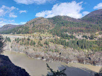 The Fraser River – The river's tan, silty color is its defining characteristic throughout the Fraser Canyon. The rocky outcroppings and sparse, evergreen-dotted hills are typical of the area near Lytton, where the landscape begins to transition from lush coastal forest into a more arid, desert-like environment.