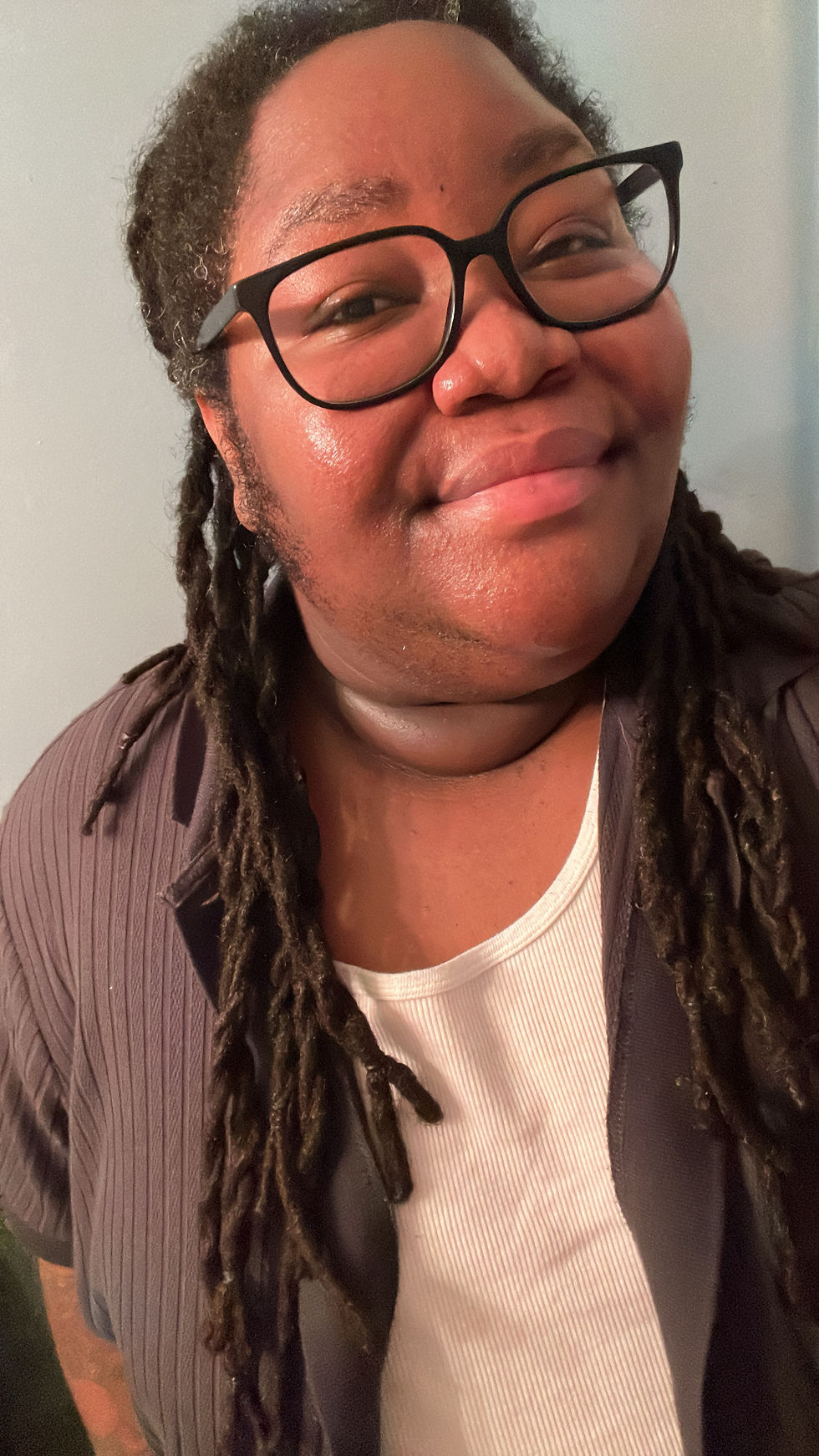 This is a picture of me smiling, wearing a black short-sleeved jacket over a white tanktop. 