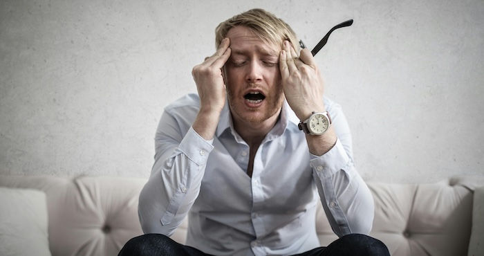 Business man rubbing his eyes from being sleepy sitting on couch. 