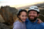 Two climbers on top of a cliff, with a rocky bluff in the background