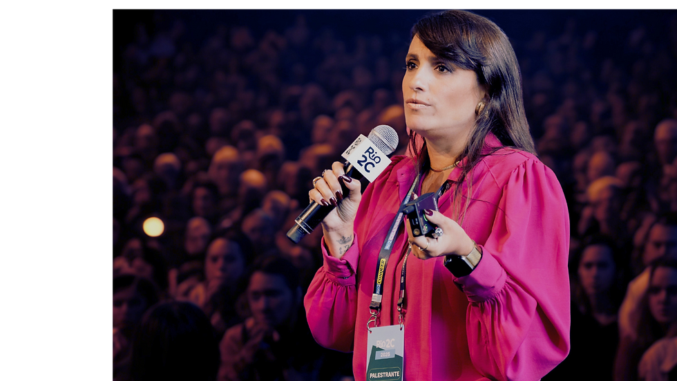 Palestrante Virgínia Chaves segurando microfone e passador de slides falando em evento com expectadores por trás.