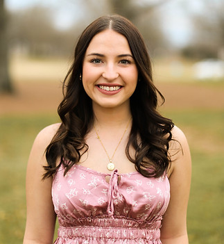 Samantha, receptionist at TRU Hair Salon — Colorado Springs luxury hair salon — smiling warmly outdoors with long dark brunette waves and a delicate gold initial necklace.