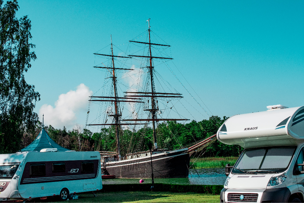 Foto di un camper e una roulotte posteggiati vicino ad un veliero