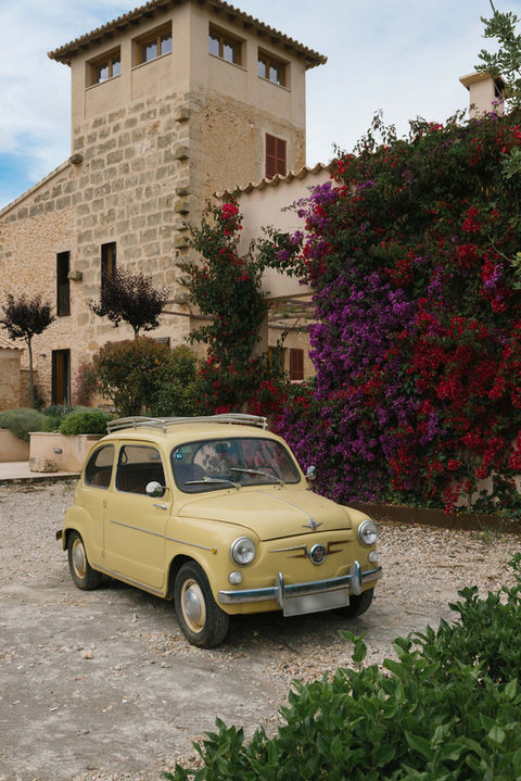 Vintage yellow seat car in front of stone house covered with vibrant bougainvillea.
