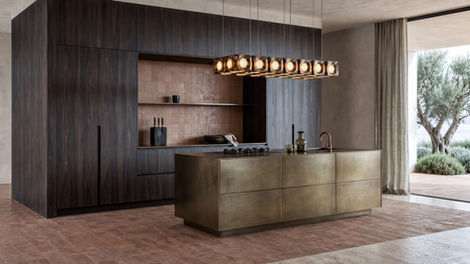 Contemporary kitchen conceived for Ibiza with dark walnut cabinetry, a monolithic bronze island and terracotta flooring.