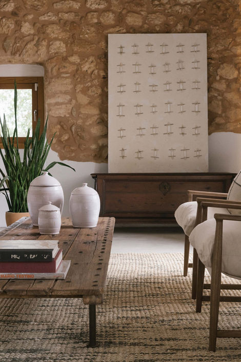 Rustic living room with stone wall, wooden coffee table, ceramic vases, and minimalist artwork.