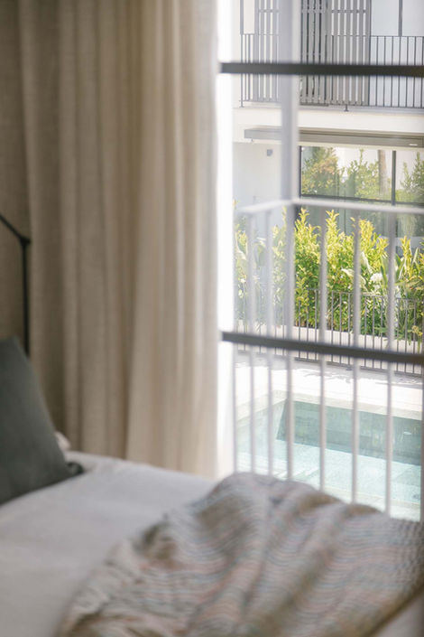 Soft view from bedroom through curtains towards a sunlit pool — Interior Design Mallorca by suō