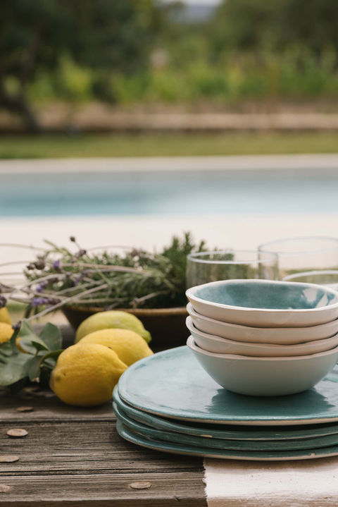 Stacked turquoise artisanal tableware with fresh lemons and Mediterranean herbs, poolside in Mallorca.