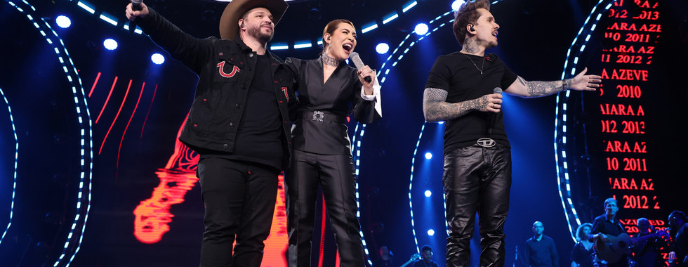 Artistas convidados participam da gravação do projeto Naiara15 ao lado de Naiara Azevedo no palco, durante apresentação ao vivo com iluminação de show e atmosfera festiva celebrando os 15 anos de carreira da cantora.