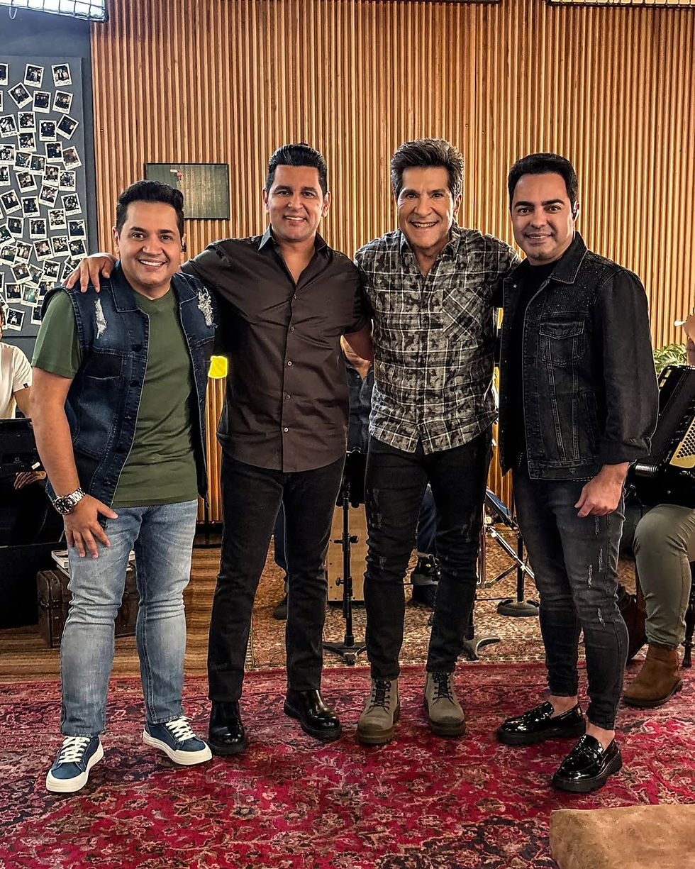 Daniel posa sorridente ao lado de Cleiton & Camargo e Léo Magalhães no cenário do programa Viver Sertanejo, com instrumentos musicais e decoração rústica ao fundo.
