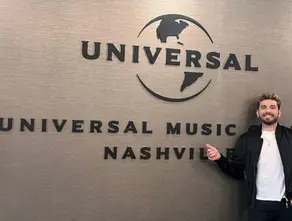 Gustavo Mioto sorrindo em frente ao letreiro da Universal Music Nashville, nos Estados Unidos, durante visita à gravadora para alinhar projeto internacional.