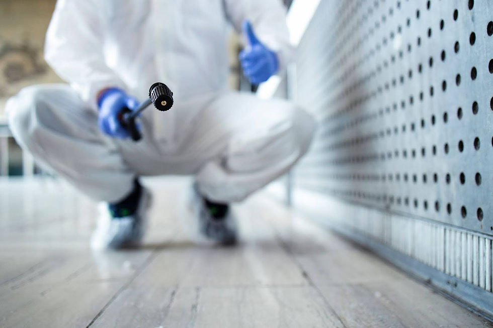 Professional remediation team in protective gear and gloves crouches near a wall, skillfully holding a spraying device for black mold remediation. The perforated metal surface of the wall looms, with the spray nozzle in focus—essential for removing mold from walls effectively.,