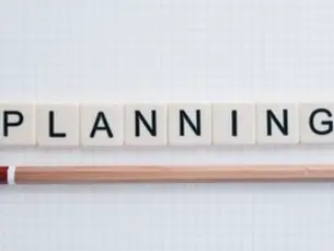 A pencil and word tiles on a grid sheet of paper. The word tiles spell "PLANNING"