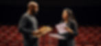 two actors - one black male, one south asian female - stand on a stage rehearsing with scr