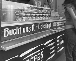 Schwarz-weiß Nahaufnahme von unserem Crêpeanhänger mit Details und Beschriftung und Zutaten hinter dem Austellungsglas.