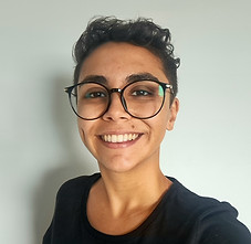 Mulher parda, com cabelo curto, na cor castanho escuro, com camiseta preta e óculos de grau com armação redonda na cor preta.