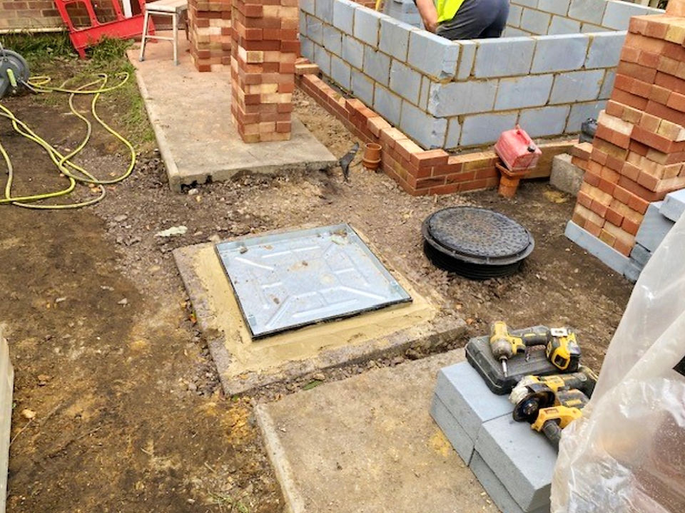 A brick extension being built with a manhole cover and construction materials.