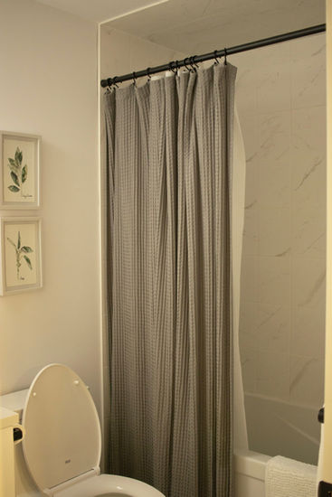 Small bathroom with gray shower curtain, toilet, and wall art