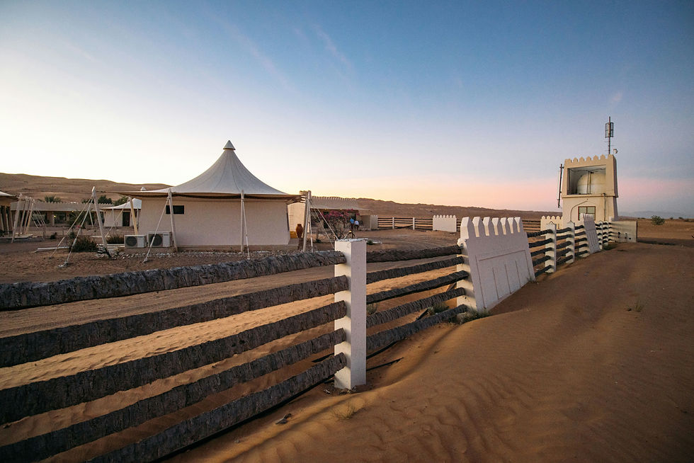 Desert camp with white tents and fence at sunset.