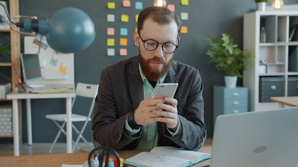 A person using a smartphone at a desk with a laptop.
