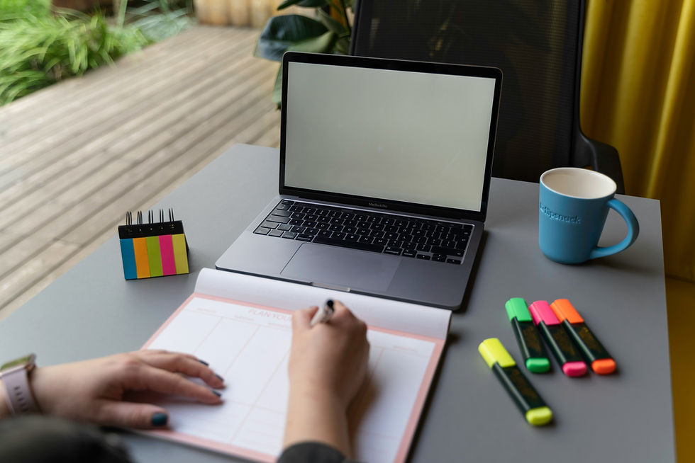 Person writing a plan on a desk with laptop, mug and markers