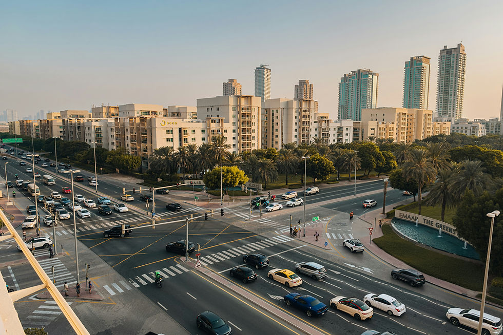 An elevated view of a busy intersection at The Greens in Dubai, with cars, pedestrian crossings and landscaped residential buildings in warm afternoon light.
