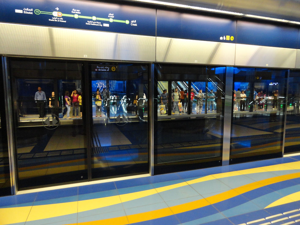 Commuters at a Dubai Metro platform behind glass screen doors.