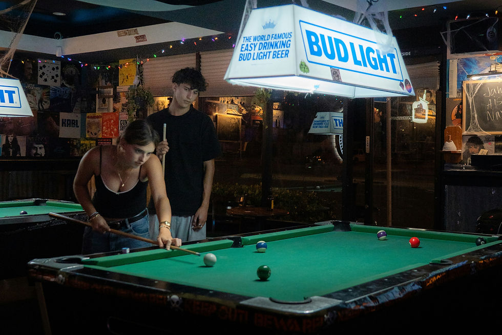 Two people playing pool under a bud light sign.
