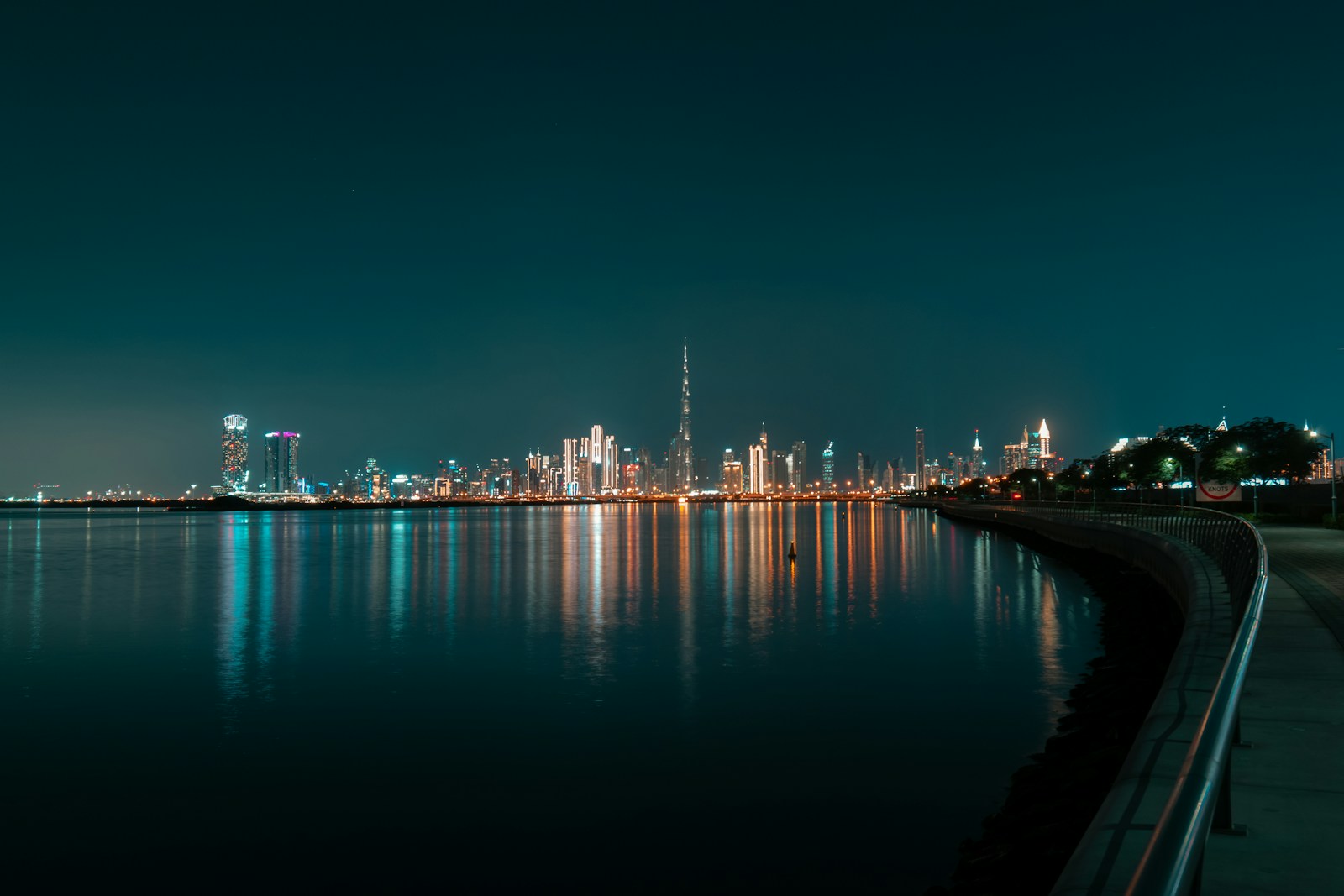 Dubai city skyline at night reflected across still water — Burj Khalifa visible in the distance