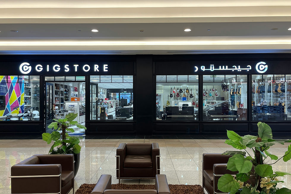 The exterior view of a sleek, contemporary Gigstore in a bright, indoor shopping mall environment. The facade is predominantly black with the illuminated white logo in both English and Arabic. Inside