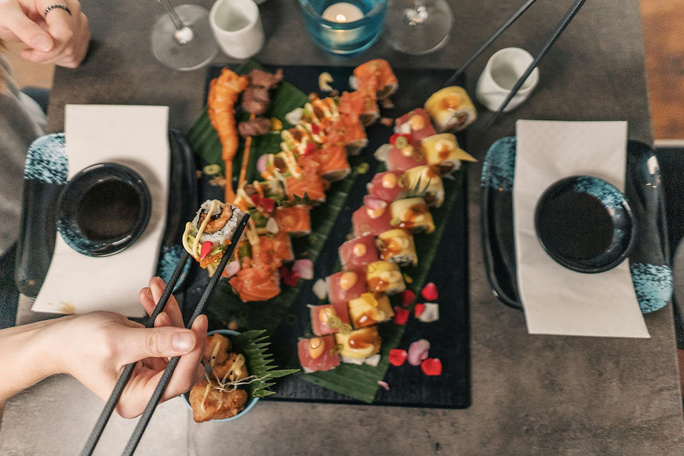 An overhead view of a sushi platter on a slate board with chopsticks and small dipping bowls