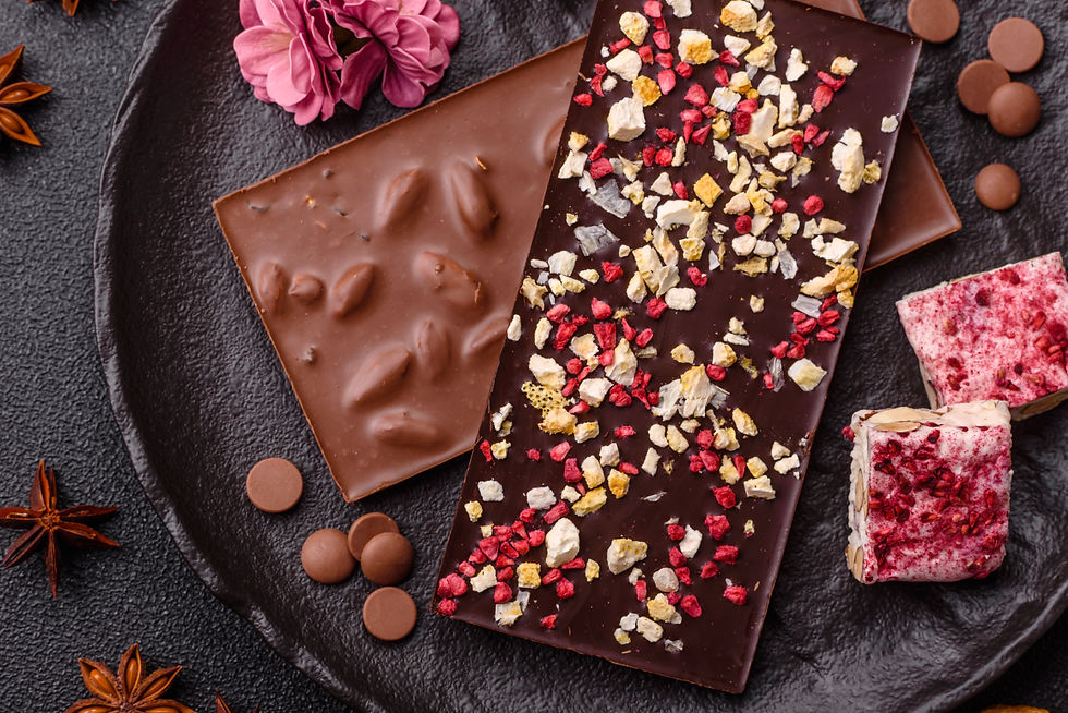Drei Tafeln Schokolade mit Nüssen und roten Crumbles auf schwarzem Teller, dekoriert mit rosa Blüte und Sternanis.