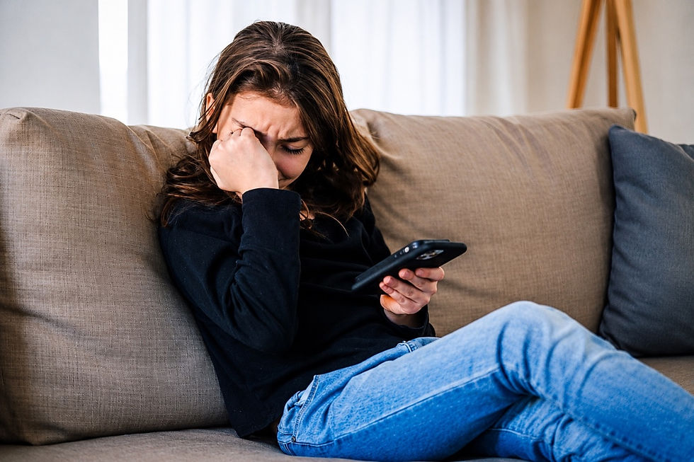 The picture shows a girl holding her mobile and her hand to her face while crying