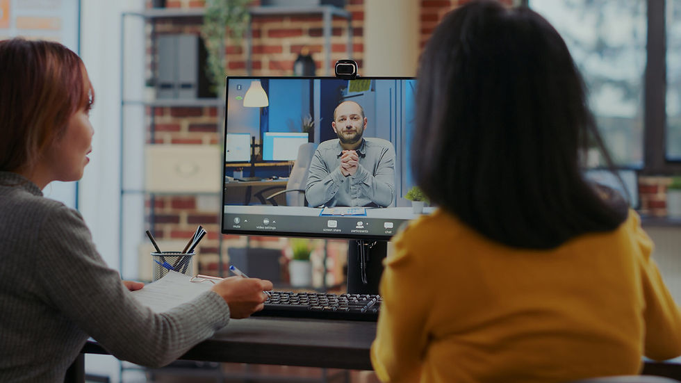 Two women virtually interview man on large computer screen.