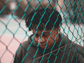 man-in-gray-hoodie-standing-beside-chain-link-fence