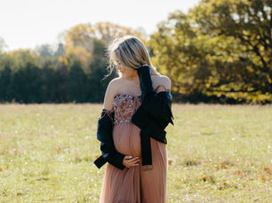 Close-up of hands resting on a pregnant belly, wedding rings visible, soft natural light highlighting textures and details.
